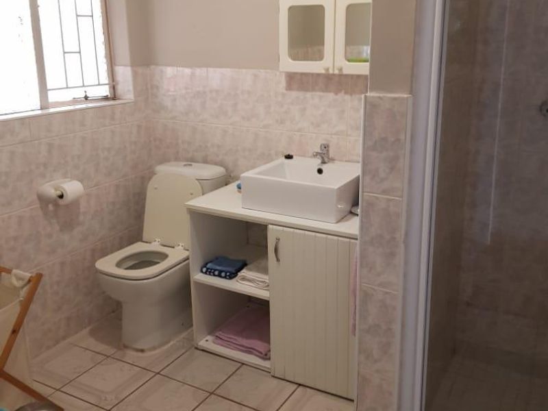 A functional bathroom featuring a shower enclosure, vanity cabinet with basin, and toilet, finished with neutral wall and floor tiling.