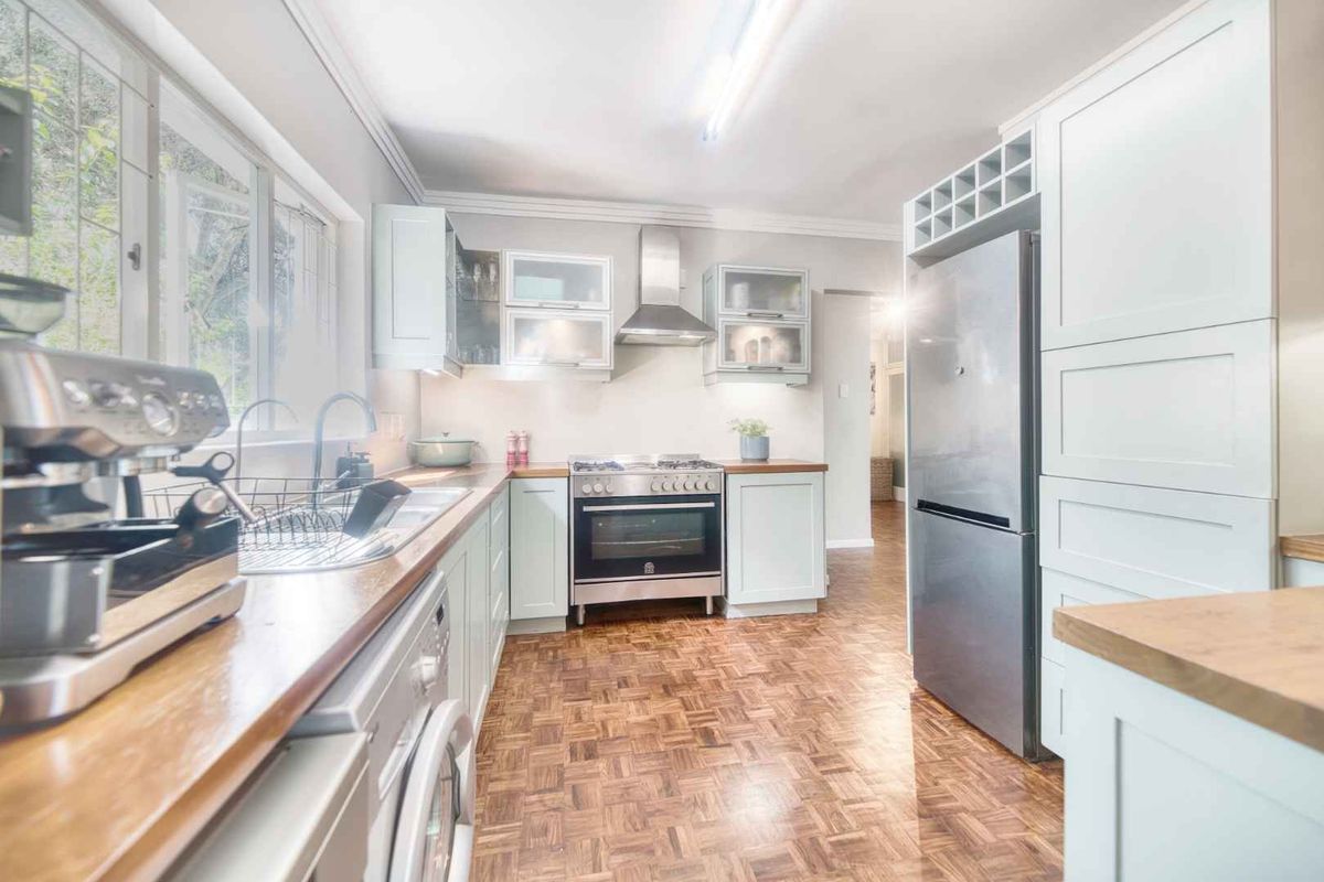 A well-maintained kitchen featuring light-toned cabinetry, wooden countertops, stainless steel appliances, and classic parquet flooring.