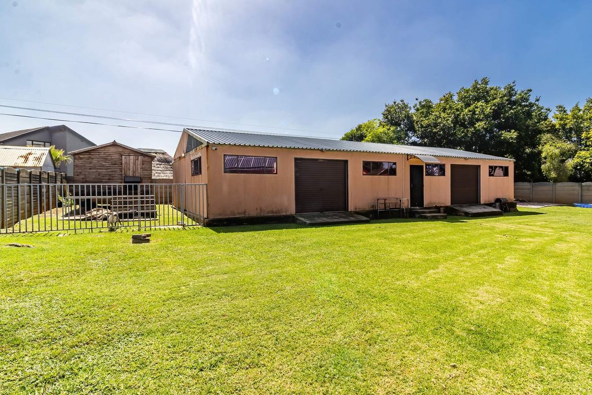 A spacious backyard featuring a large detached garage building with multiple roller doors and a well-maintained lawn area.