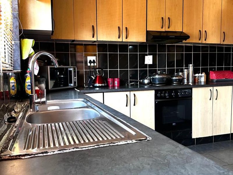 A functional kitchen featuring laminate cabinetry, a stainless steel double sink, black tiled backsplash, and built-in oven with extractor fan.