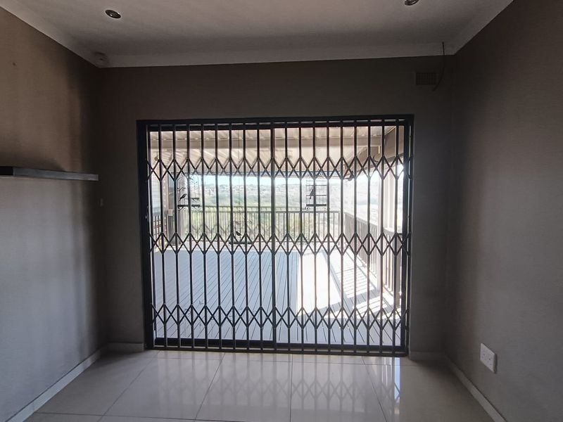 An empty living room featuring tiled floors, recessed lighting, and a retractable security gate leading to an outdoor balcony area.