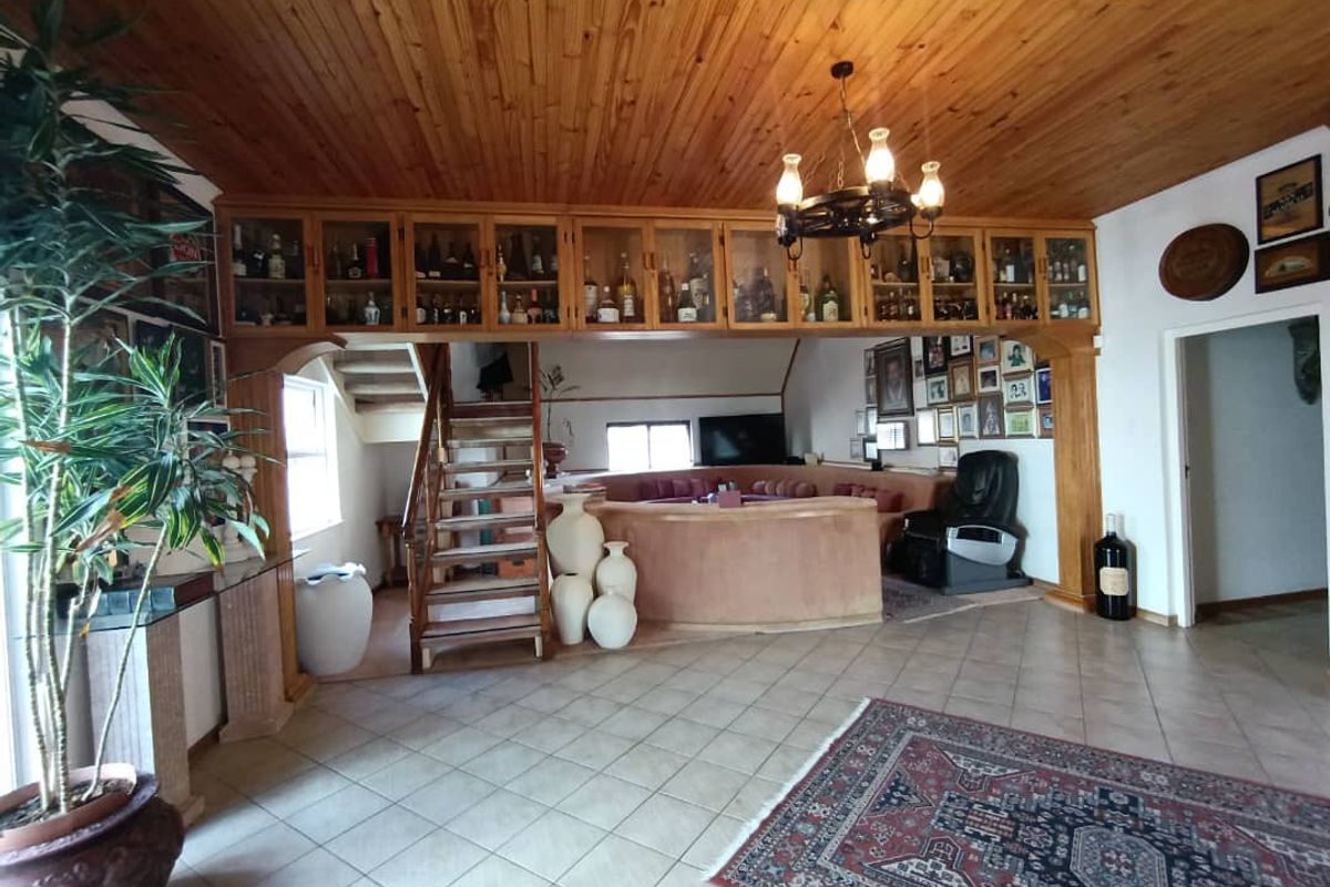 Spacious living area featuring a timber ceiling, built-in bar cabinetry, and a staircase leading to an upper level with tiled flooring throughout.