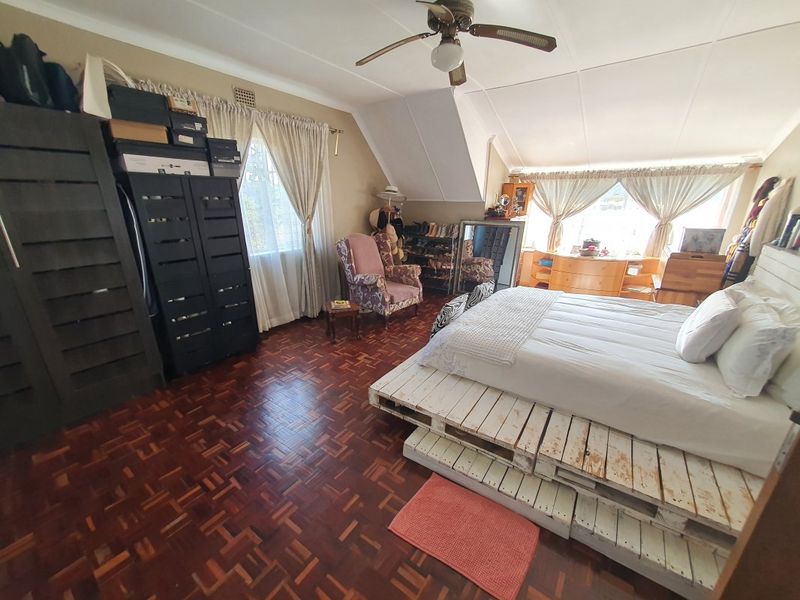 Spacious bedroom featuring classic parquet flooring, a ceiling fan, and a unique sloped ceiling design with ample natural light.