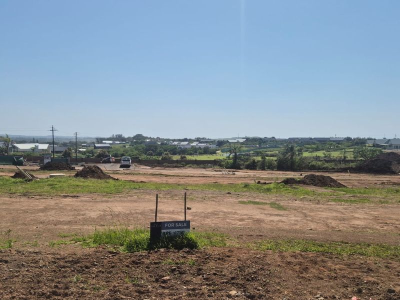 A wide-angle view of a vacant residential plot of land in a developing estate, featuring a for sale sign and surrounding neighborhood views.