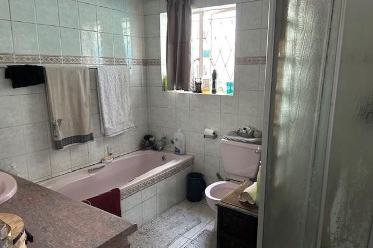 A dated bathroom featuring a pink bathtub and toilet, tiled walls, and a separate shower enclosure with a window for natural light.