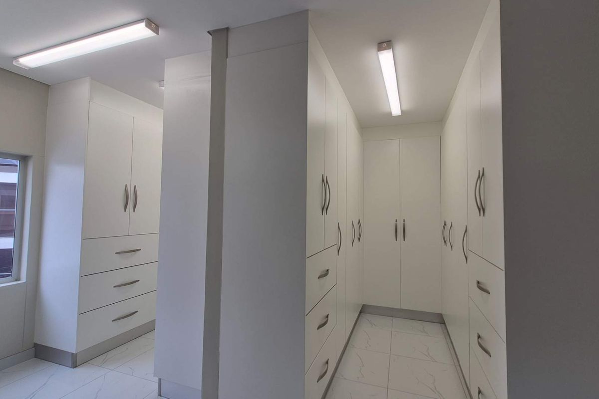 A clean and modern walk-in closet area featuring extensive white built-in cabinetry, tiled flooring, and bright overhead lighting.