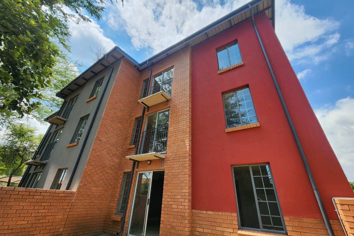 Exterior view of a multi-story apartment building featuring a combination of red brick and painted facade, balconies, and sliding glass doors.