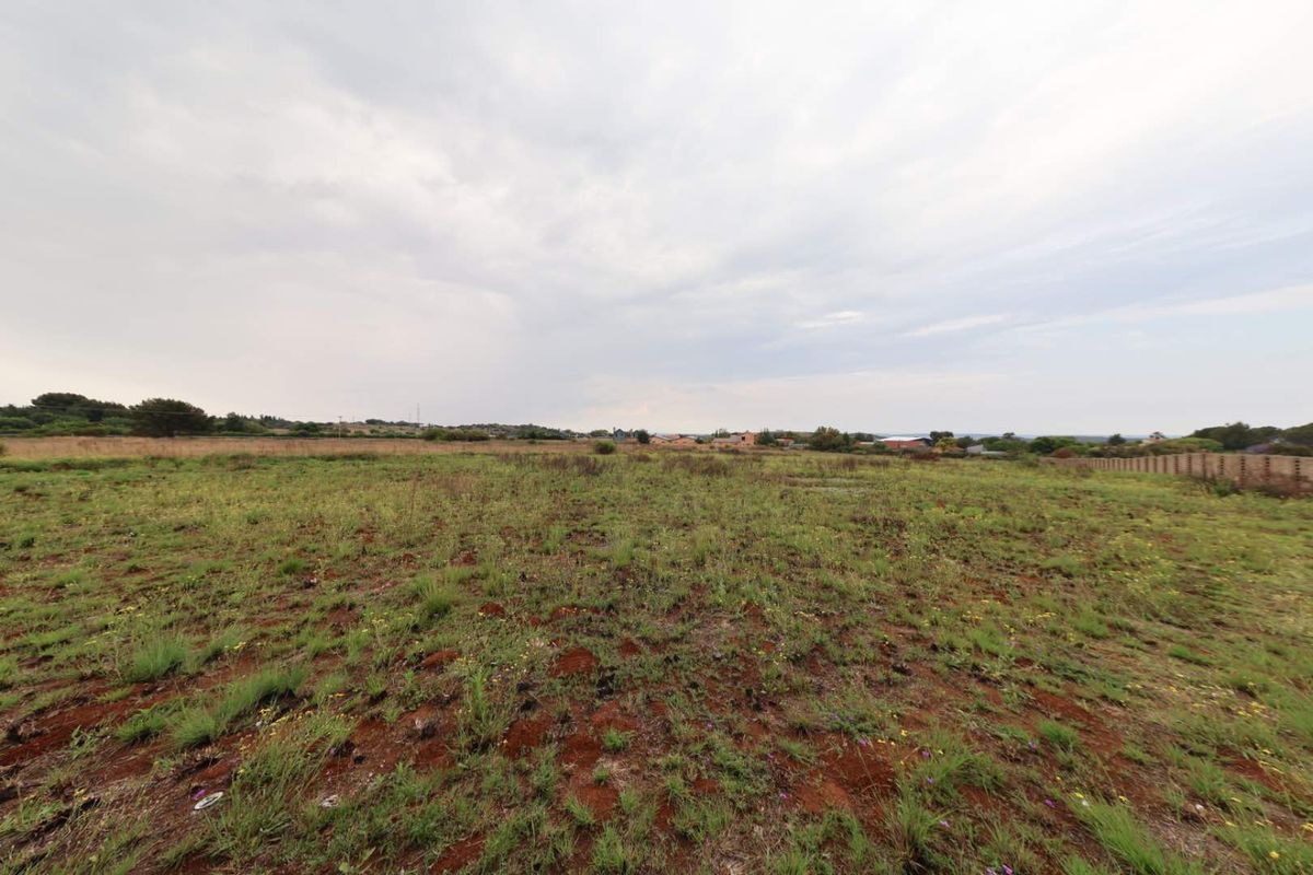 A wide-angle view of a vacant residential plot featuring natural vegetation and perimeter fencing, offering a blank canvas for future development.