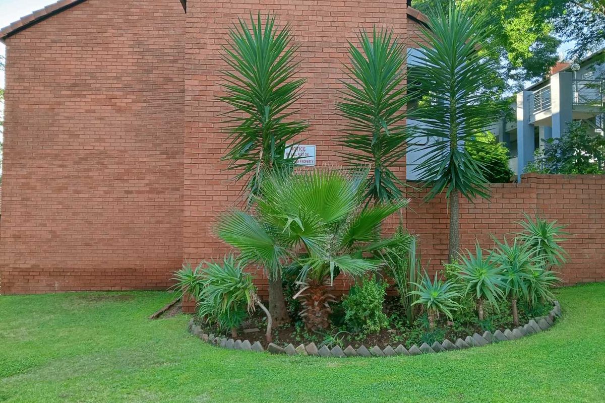 A view of the apartment building's exterior rear facade featuring a well-maintained brick wall and landscaped garden area.