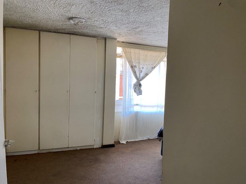 A vacant bedroom featuring built-in cupboards, textured ceiling, and carpeted flooring, offering a blank canvas for potential renovation and modernization.