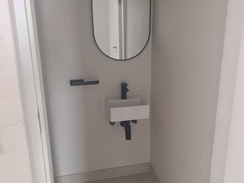 A compact, modern guest powder room featuring a minimalist wall-mounted basin, black fixtures, and a sleek oval mirror.