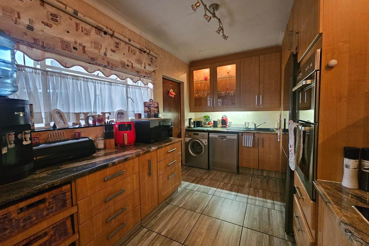 A functional kitchen featuring wood-veneer cabinetry, integrated oven, built-in dishwasher, and tiled flooring with ample counter space.