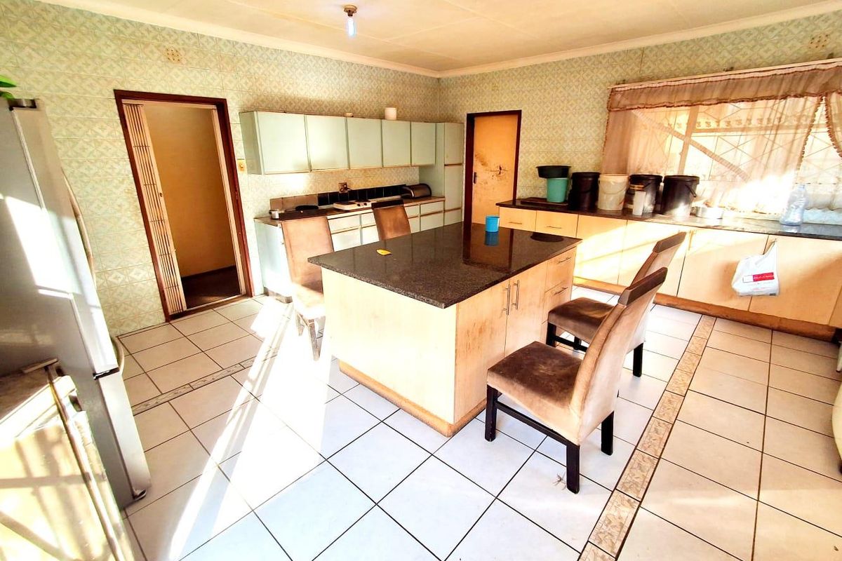A dated kitchen featuring a central island with granite countertop, ample cabinetry, and tiled flooring, offering a functional layout with potential for modernization.