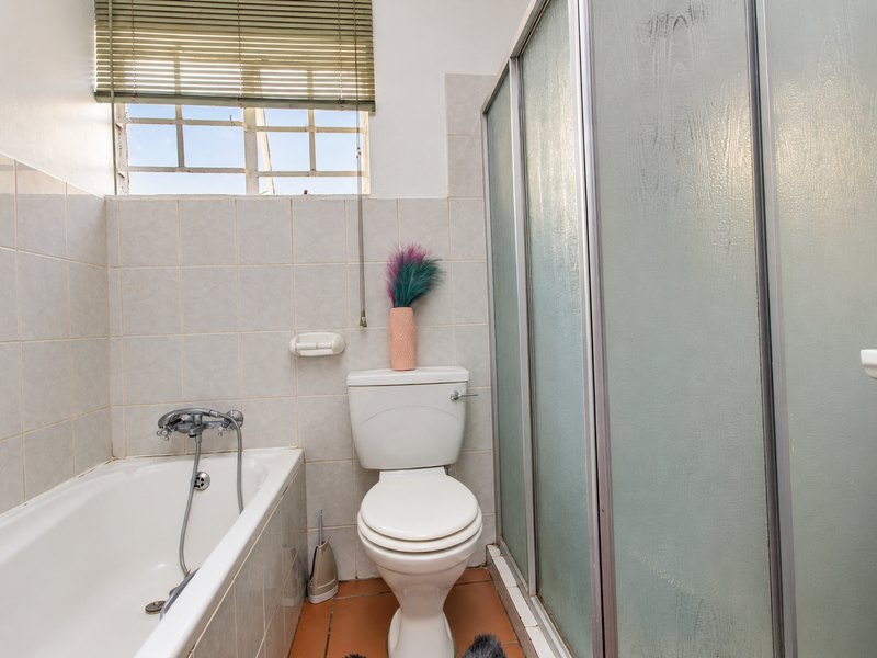 A functional bathroom featuring a bathtub, separate shower enclosure, and toilet, finished with neutral wall tiles and tiled flooring.