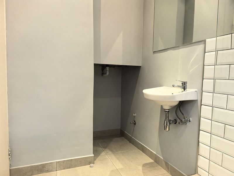 A minimalist bathroom featuring a wall-mounted basin, subway tile accents, and a large mirror, currently awaiting final finishing touches to the plumbing area.