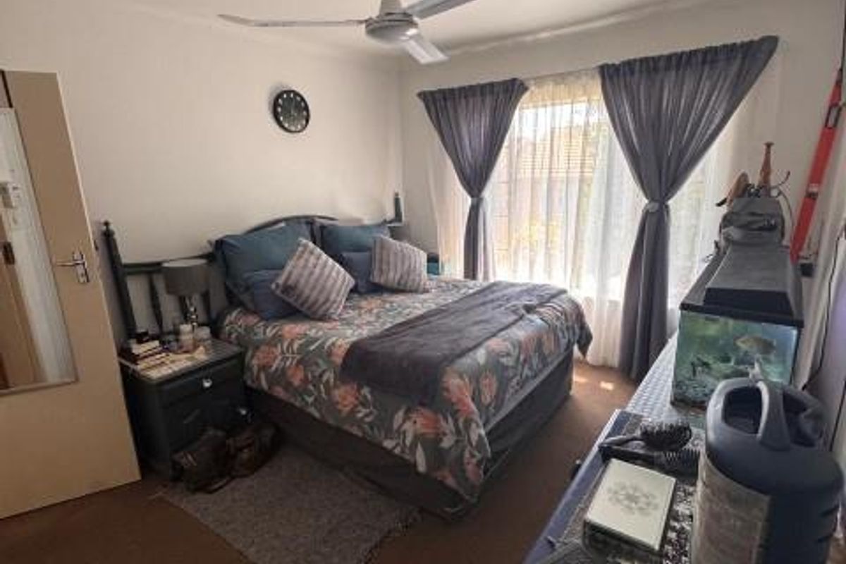 A functional bedroom featuring a ceiling fan and large windows with curtain rails, providing natural light and a comfortable living space.