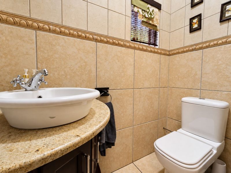 A compact bathroom featuring beige ceramic wall tiles, a granite vanity countertop with a vessel sink, and a modern toilet.