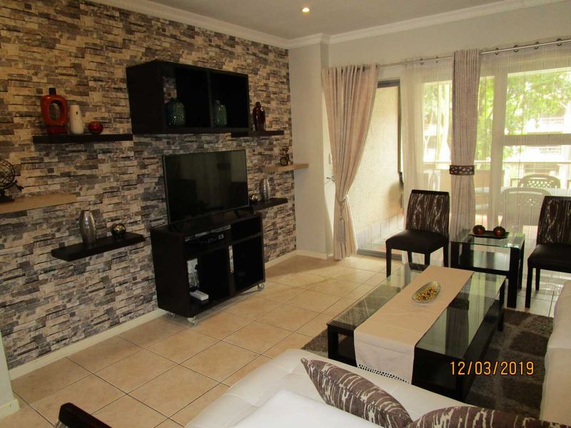 A living room featuring a stone veneer accent wall, ceramic tiled flooring, and large sliding glass doors providing access to an outdoor balcony area.
