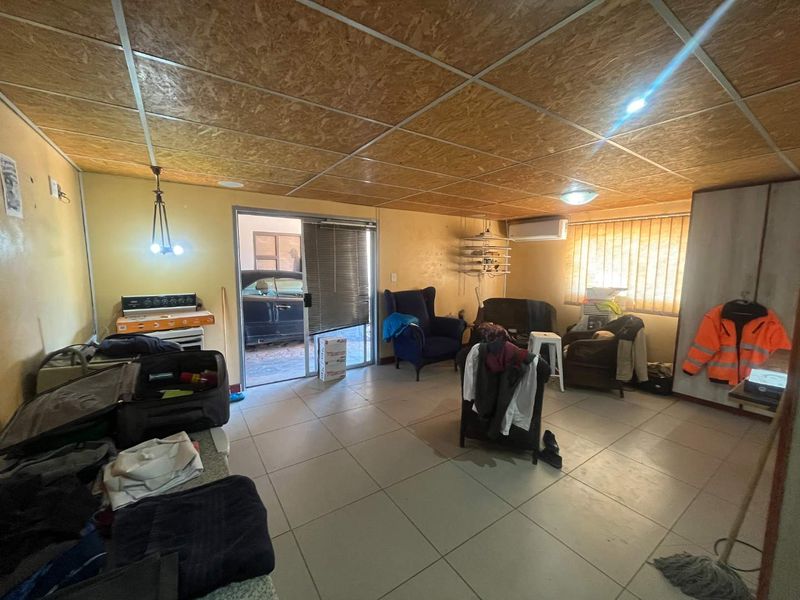 Open-plan living area featuring tiled flooring, OSB ceiling panels, and a sliding door leading to an exterior space, with an integrated air conditioning unit.