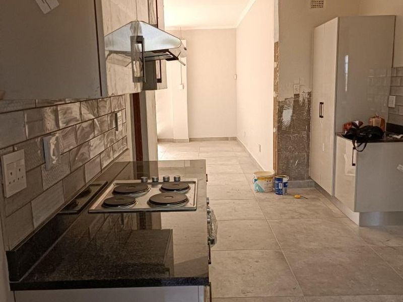 A kitchen area featuring modern cabinetry and granite countertops, currently undergoing renovation with unfinished wall sections and exposed plaster.