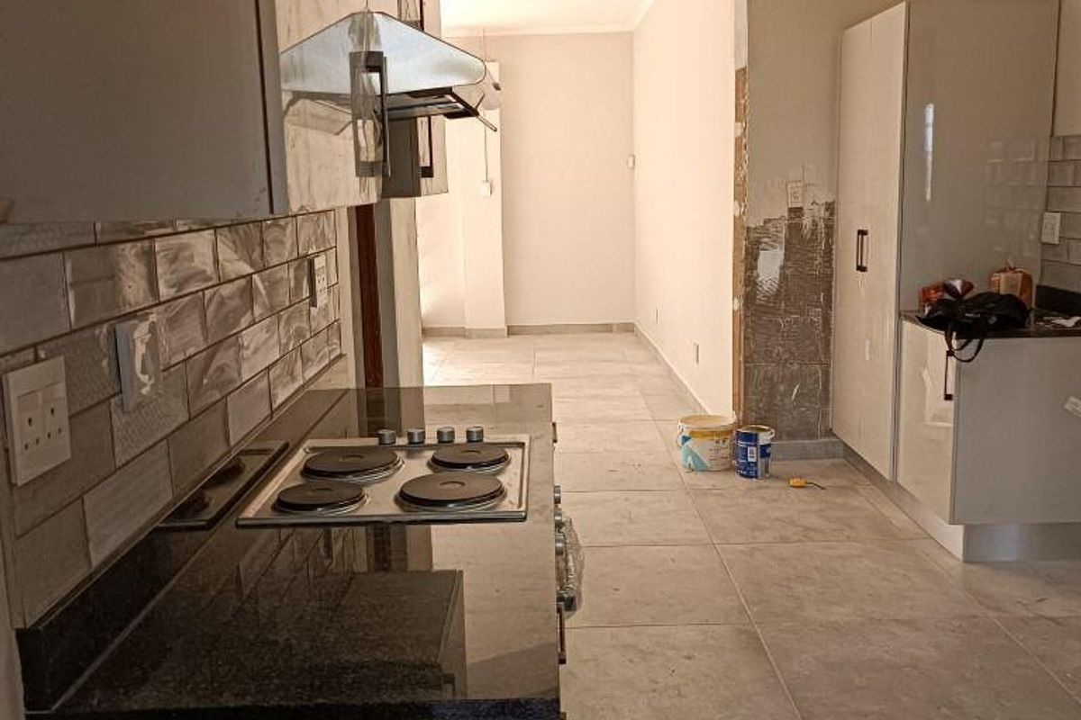 A kitchen area featuring modern cabinetry and granite countertops, currently undergoing renovation with unfinished wall sections and exposed plaster.
