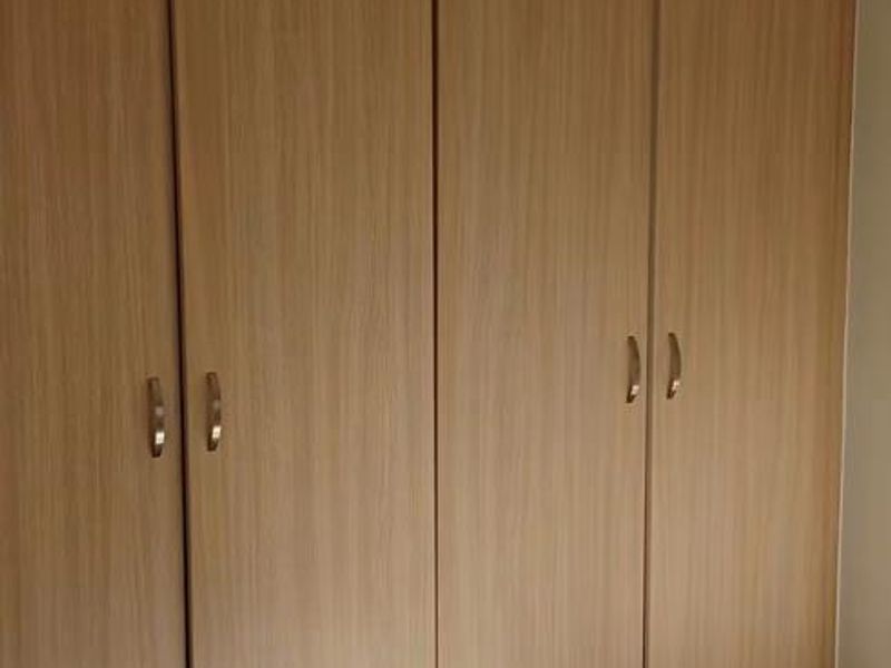 A bedroom featuring light wood-finish built-in cupboards and neutral floor tiles, offering a clean and functional storage solution.