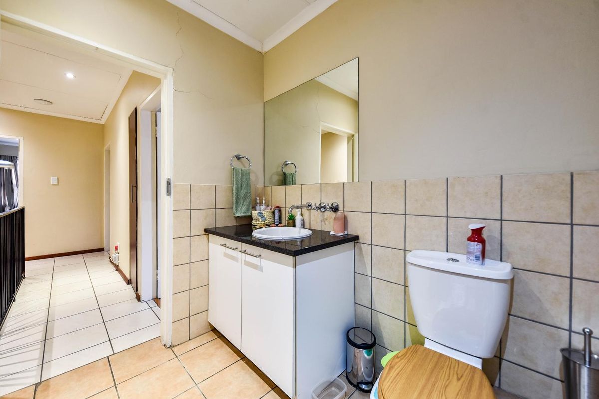 A functional bathroom featuring a vanity cabinet with a basin, wall-mounted faucet, mirror, and toilet, finished with tiled splashbacks and flooring.