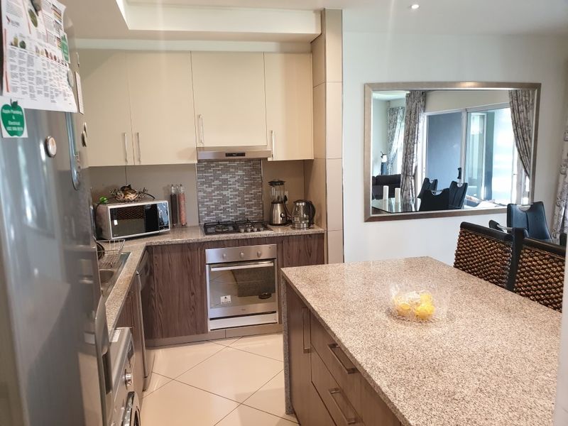 Modern kitchen featuring granite countertops, built-in oven, gas hob, extractor fan, and a central island, seamlessly flowing into the adjacent living area.