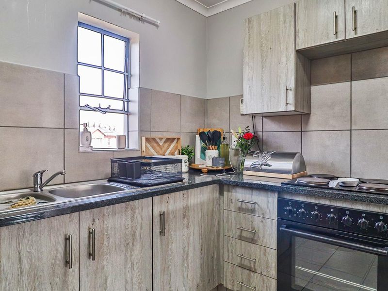 A functional kitchen featuring wood-look laminate cabinetry, granite countertops, a stainless steel sink, and a built-in oven with an electric hob.