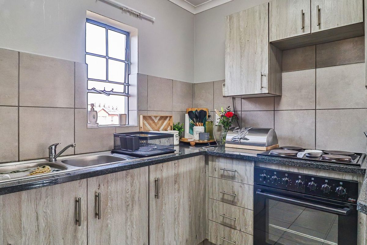 A functional kitchen featuring wood-look laminate cabinetry, granite countertops, a stainless steel sink, and a built-in oven with an electric hob.