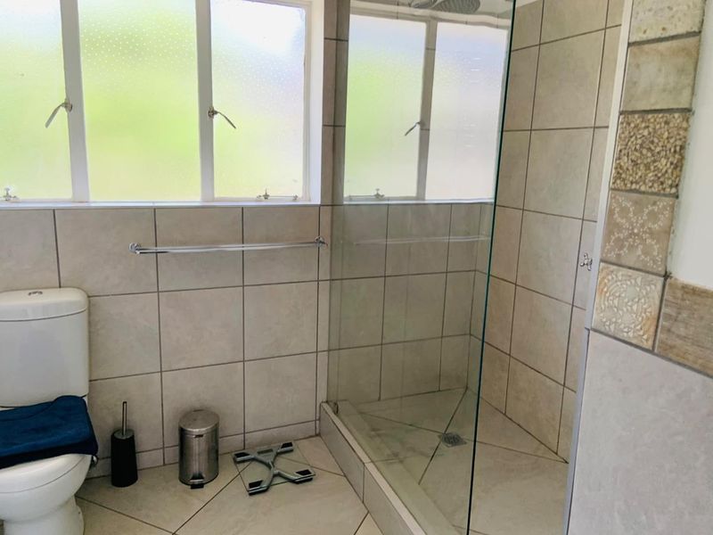 A functional bathroom featuring a glass-enclosed shower, tiled flooring, and wall tiling, providing a clean and practical space.