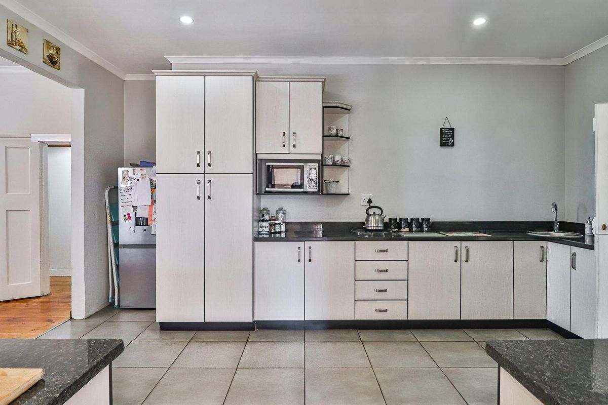 A functional kitchen featuring light-toned cabinetry, dark laminate countertops, built-in microwave, and tiled flooring with recessed lighting.