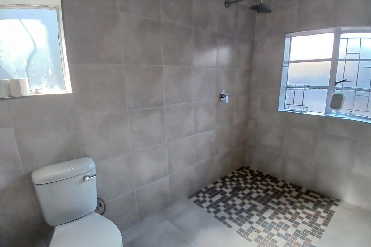 A functional bathroom featuring a walk-in shower with mosaic floor tiling, a wall-mounted shower head, and a standard toilet.