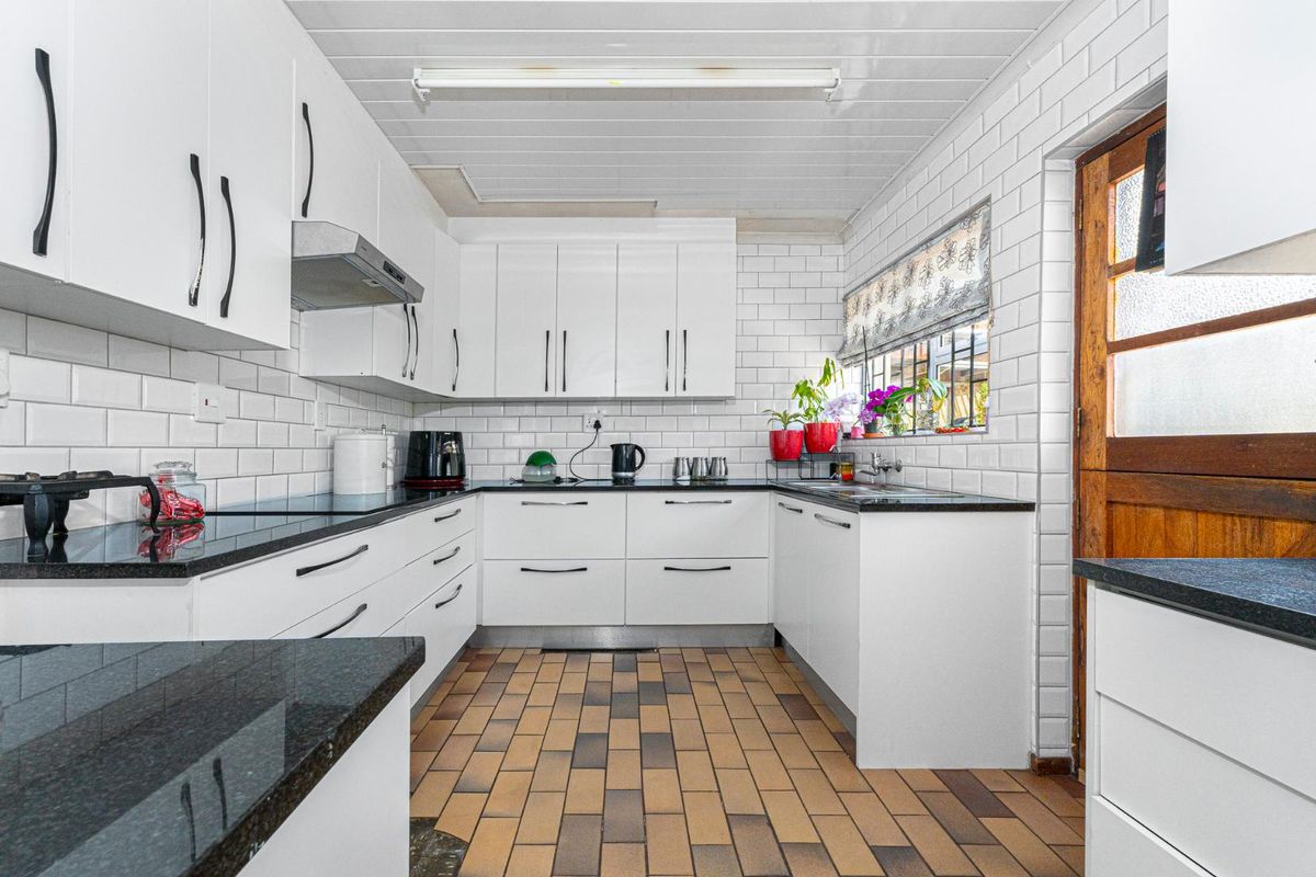 A functional kitchen featuring white cabinetry, dark granite countertops, subway tile backsplash, and a tiled floor with direct exterior access.