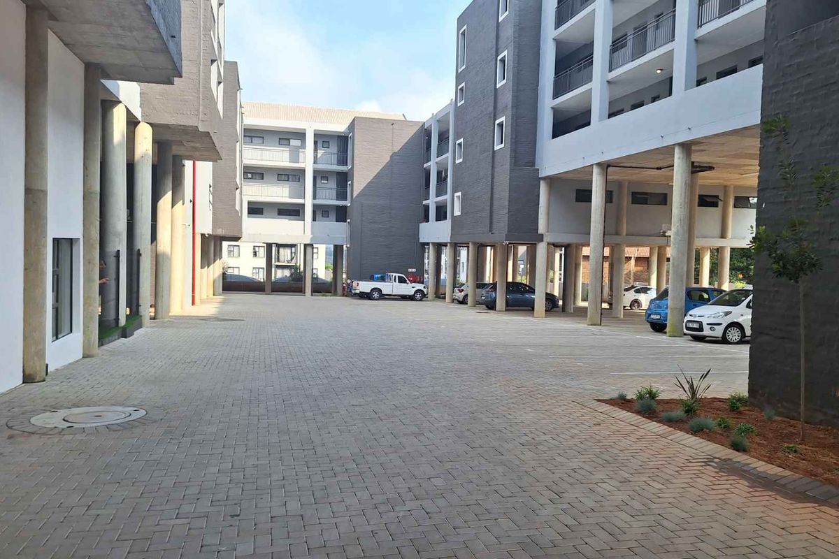 A view of the paved courtyard and covered parking area between modern multi-story apartment blocks.