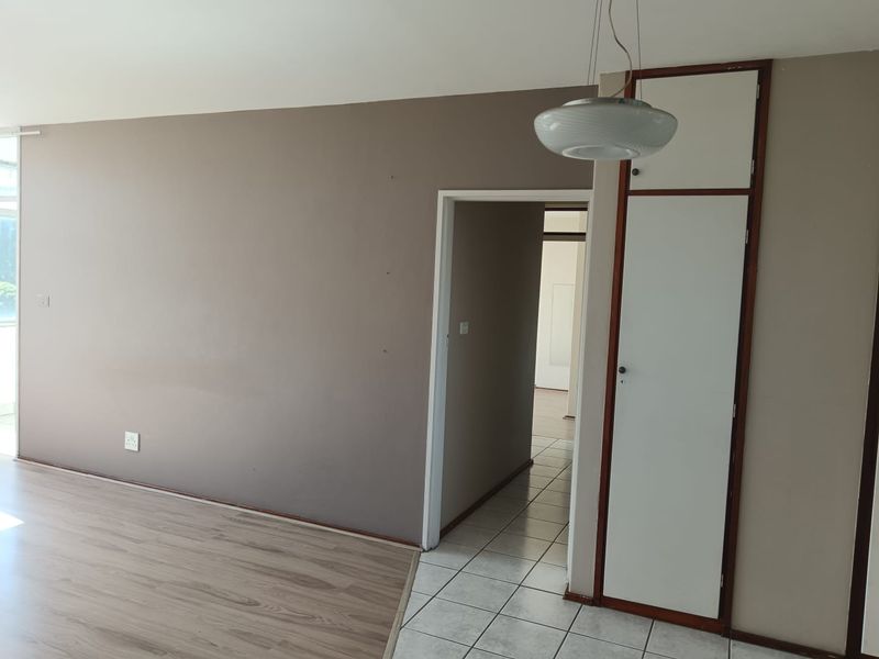 An empty living area featuring a mix of laminate and tiled flooring, a built-in storage cupboard, and neutral wall tones.