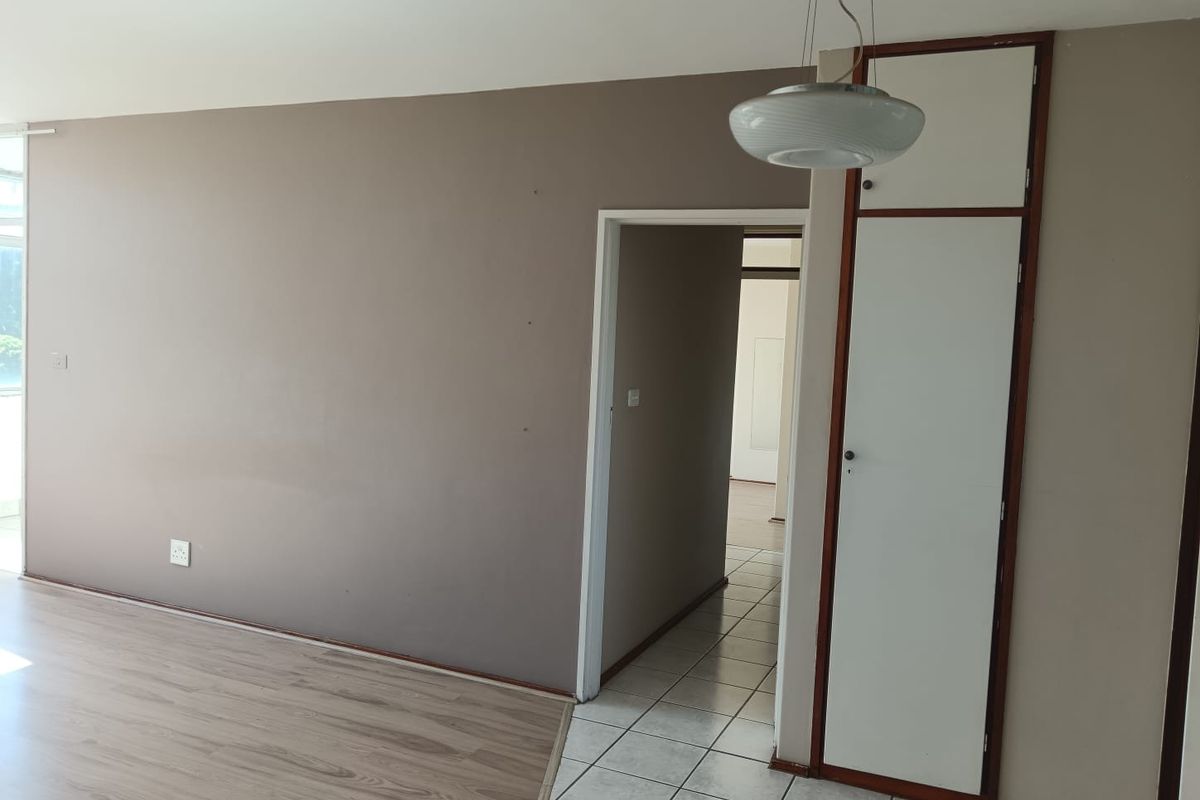 An empty living area featuring a mix of laminate and tiled flooring, a built-in storage cupboard, and neutral wall tones.