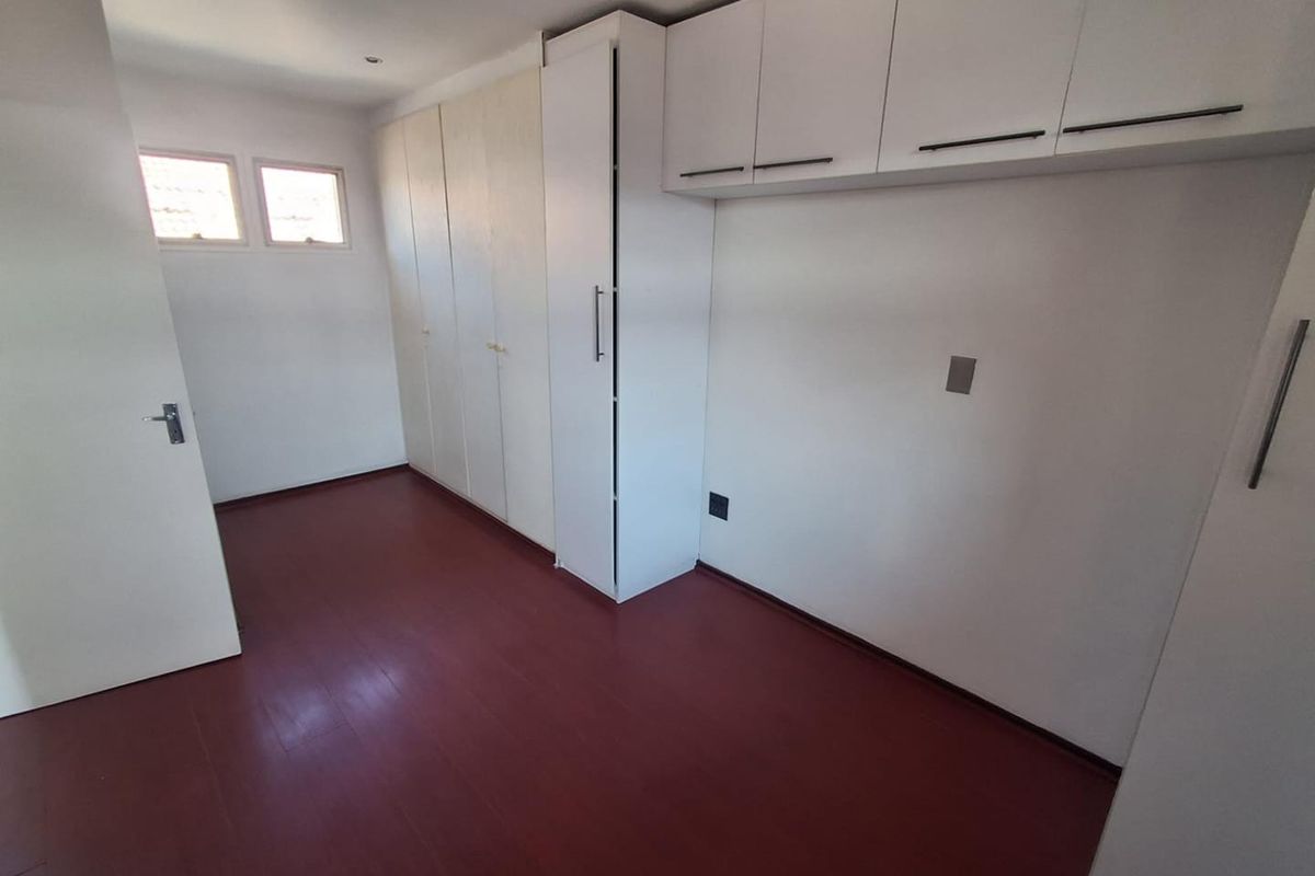 A bedroom featuring built-in floor-to-ceiling cabinetry and overhead storage units, finished with dark-toned flooring and neutral walls.