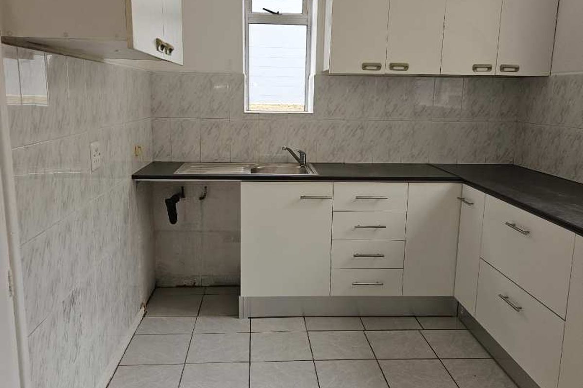 A functional, empty kitchen featuring white cabinetry, dark laminate countertops, tiled backsplash, and tiled flooring, ready for modernization.