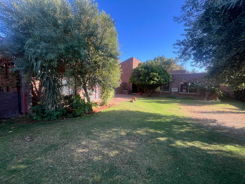 A spacious rear garden featuring a well-maintained lawn, mature trees, and a classic brick exterior facade with security bars on the windows.