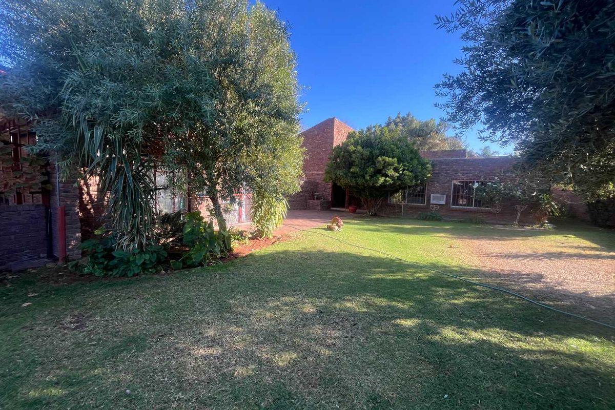 A spacious rear garden featuring a well-maintained lawn, mature trees, and a classic brick exterior facade with security bars on the windows.