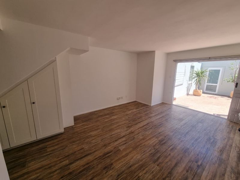 Bright and spacious living area featuring modern laminate flooring and convenient under-stair storage, with direct access to an outdoor patio area.