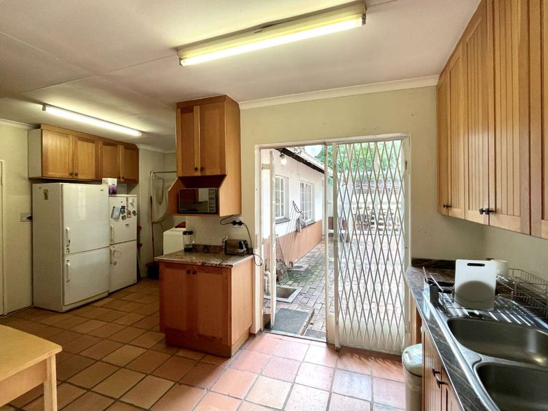 A functional kitchen featuring wooden cabinetry, laminate countertops, double sink, and tiled flooring, with direct access to an outdoor paved area.