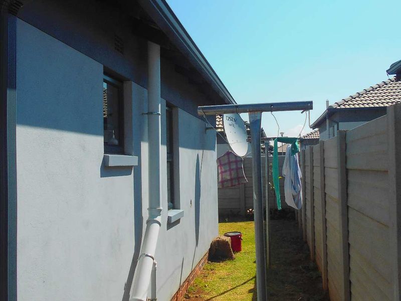 A side exterior view of the property featuring a precast concrete boundary wall, downpipe, and a metal washing line.