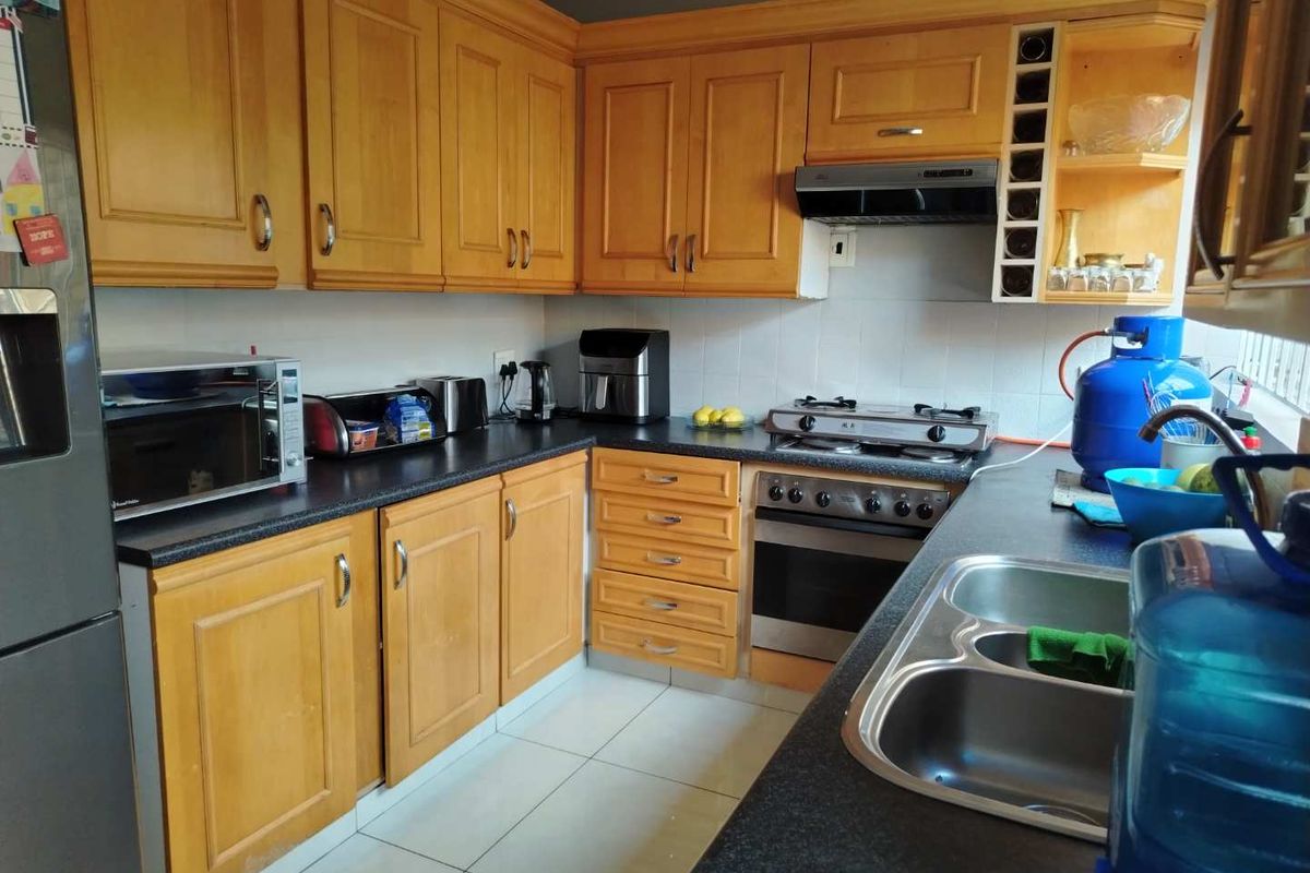 A functional kitchen featuring wooden cabinetry, dark countertops, a built-in oven with gas hob, extractor fan, and a double stainless steel sink.