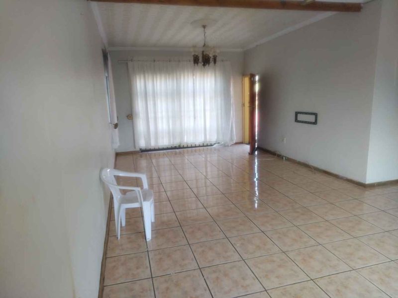A spacious, empty living area featuring tiled flooring, a ceiling rose, and an exposed wooden ceiling beam, offering a blank canvas for renovation.