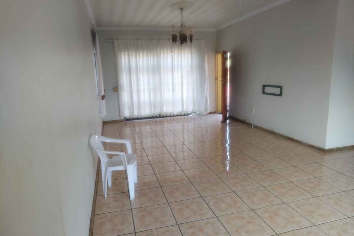 A spacious, empty living area featuring tiled flooring, a ceiling rose, and an exposed wooden ceiling beam, offering a blank canvas for renovation.