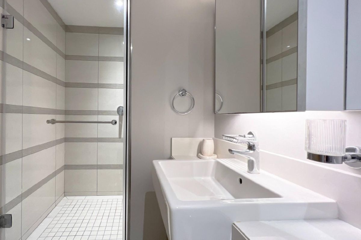 A modern, clean bathroom featuring a walk-in shower with glass enclosure, wall-mounted basin, and a mirrored medicine cabinet.