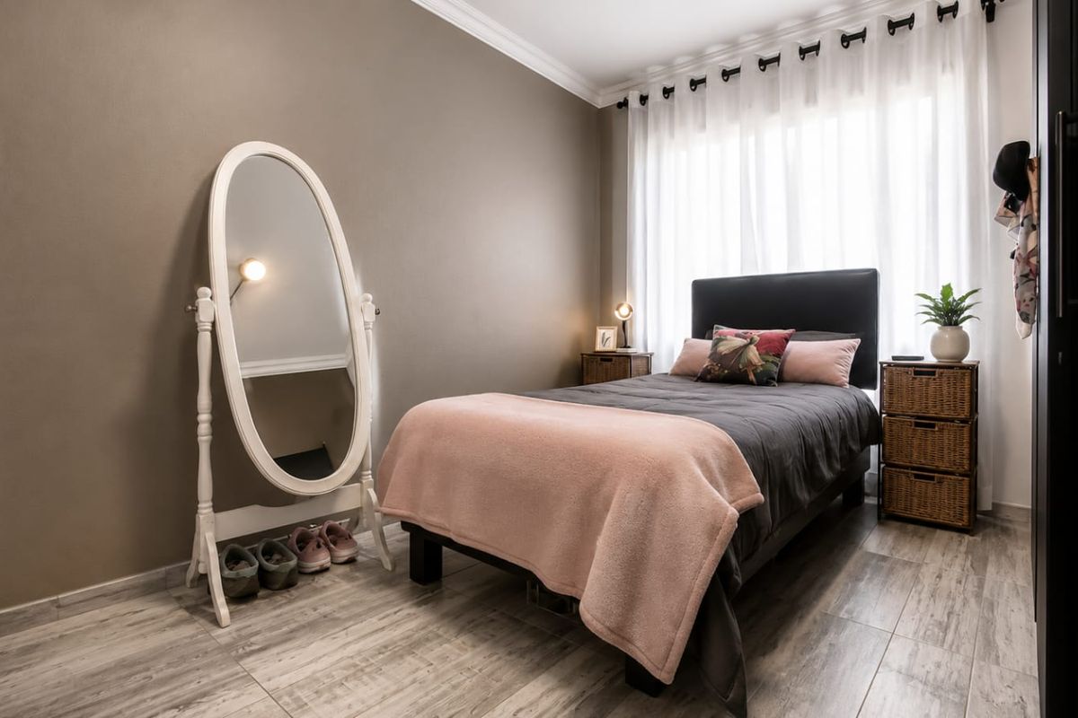 A well-maintained bedroom featuring wood-look tile flooring, crown molding, and large windows with sheer curtains, providing a bright and comfortable living space.