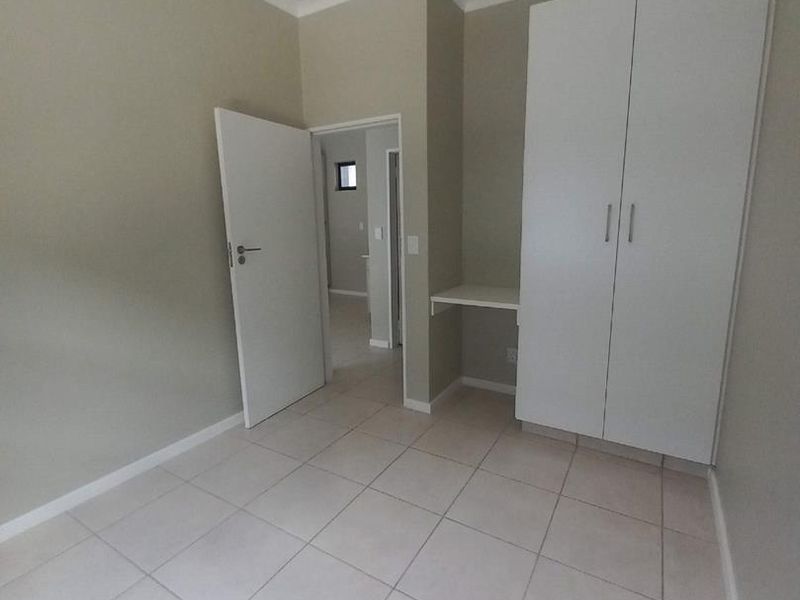 A clean, empty bedroom featuring neutral tiled flooring, a built-in wardrobe, and a small integrated desk area.